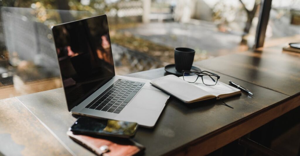 A serene office setup with a laptop, notebook, and coffee near a window, reflecting an autumn scene.